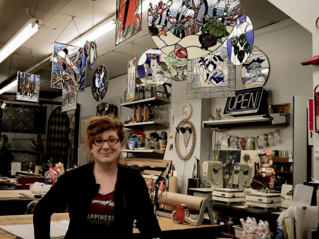 Artist standing inside a stained glass studio in St. Thomas, surrounded by colorful stained glass pieces and tools.